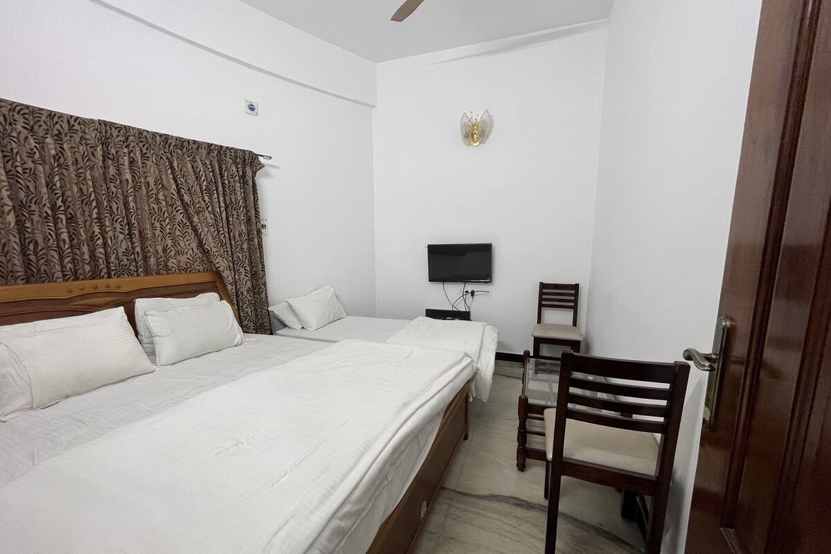 A hotel room with a bed, a desk, a chair, a television, and a ceiling fan.