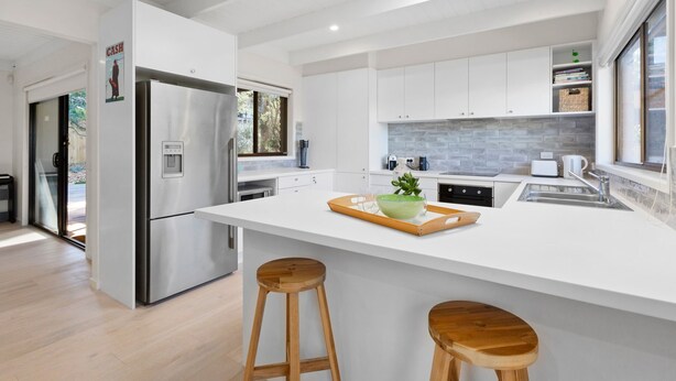A modern kitchen with white cabinetry, a stainless steel refrigerator, a large island with stools, and a view of the outdoors. - Brooks by the bay  - Blairgowrie (Blairgowrie)