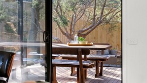 A wooden deck with a table and benches, a glass door, and a view of trees and a wooden fence. - Brooks by the bay  - Blairgowrie (Blairgowrie)