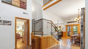 A spacious interior with a wooden staircase, a dining area with a table and chairs, and a chandelier. - 2BD + Loft, Walk-In Cabin- Discounts on Golf & Tickets! (Branson)