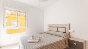 Une chambre à coucher avec un lit, une table de chevet, une fenêtre et une vue sur un immeuble jaune à l’extérieur.