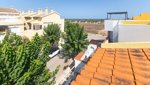 Un quartier résidentiel aux toits recouverts de tuiles en terre cuite, une rue bordée de voitures garées et, au loin, une vue dégagée sur la mer.