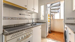 Une cuisine compacte avec des meubles blancs, un plan de travail en granit, un four encastré et une fenêtre donnant sur un balcon.