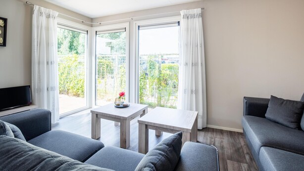 Ein modernes Wohnzimmer mit grauen Sofas, einem kleinen Holztisch und einem Fernseher auf einem Schrank.