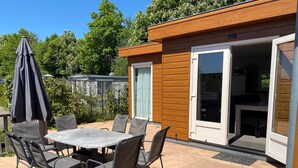 Eine Terrasse im Freien mit Tisch und Stühlen, einem beschatteten Sonnenschirm und einem Holzhaus mit einer Schiebetür.