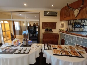 A dining area with a buffet setup, a refrigerator, and a bar area with a decorative skull. - Hôtel Les 12 Collines, Ivato Ambohijanahary (Antananarivo)