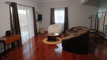 A living room with a wooden floor, a white armchair, a brown sofa, a coffee table, and a TV mounted on the wall.