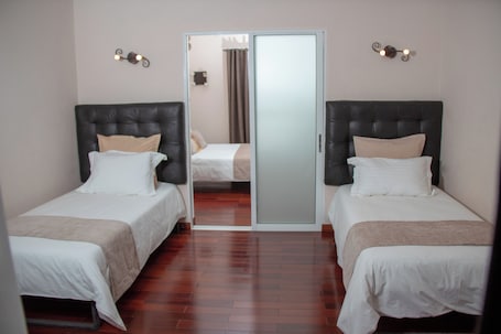 A hotel room with two single beds, a wardrobe, and a mirror.
