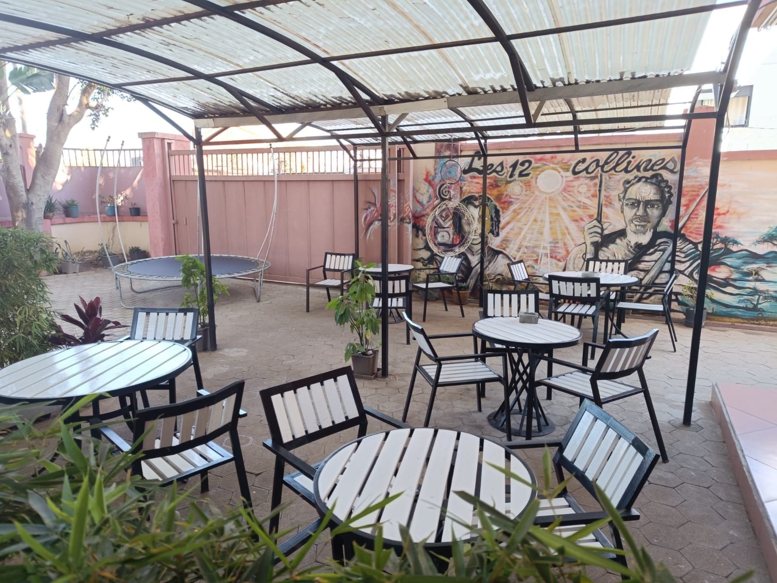 An outdoor patio area with round tables and chairs, a mural on the wall, and potted plants.