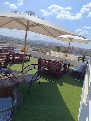 A rooftop terrace with wooden furniture, a table, and two large umbrellas. - Hôtel Les 12 Collines, Ivato Ambohijanahary (Antananarivo)