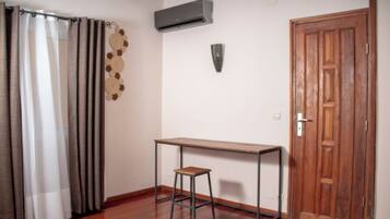 A room with a wooden floor, a small wooden table with a stool, a wooden door, and a curtain.