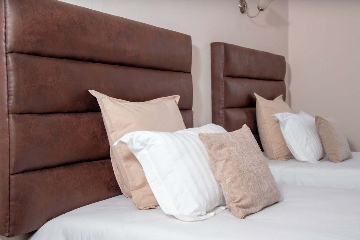 A bed with a brown headboard, white bedding, and beige pillows.