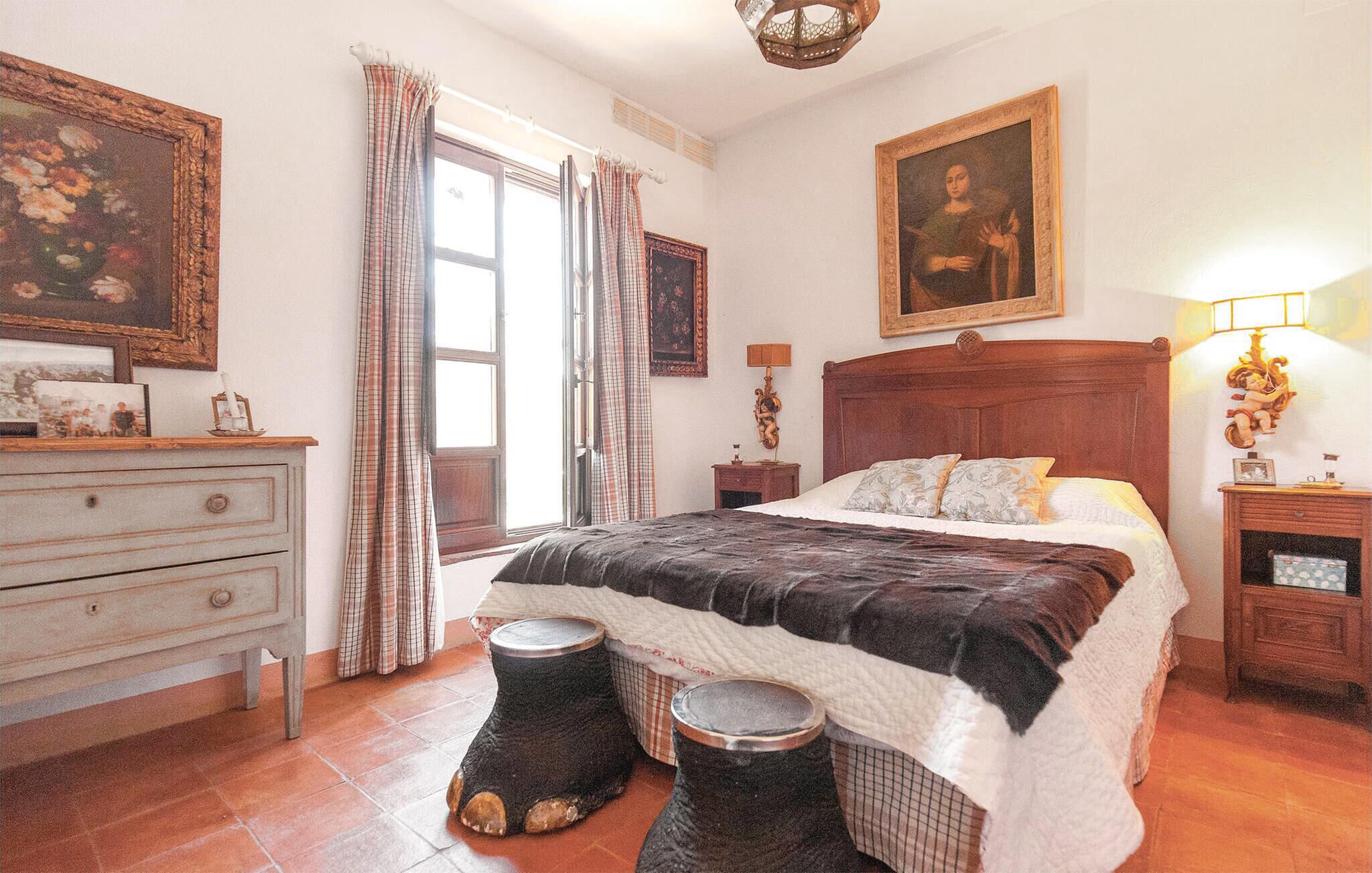 A bedroom with a large bed, a dresser, a nightstand, a lamp, and a painting on the wall.