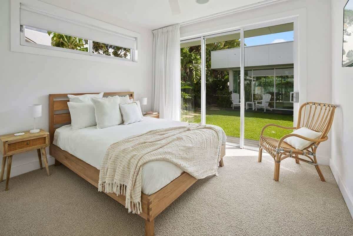 A bedroom with a large bed, a nightstand, a wicker chair, and a sliding glass door leading to a patio.