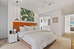 Een moderne slaapkamer met een groot bed, een nachtkastje, een plafondventilator en een kunstwerk aan de muur.
