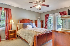 Ein Schlafzimmer mit einem hölzernen Bett, einem Nachttisch, einer Kommode, einem Deckenventilator und einem Fenster mit Vorhängen.