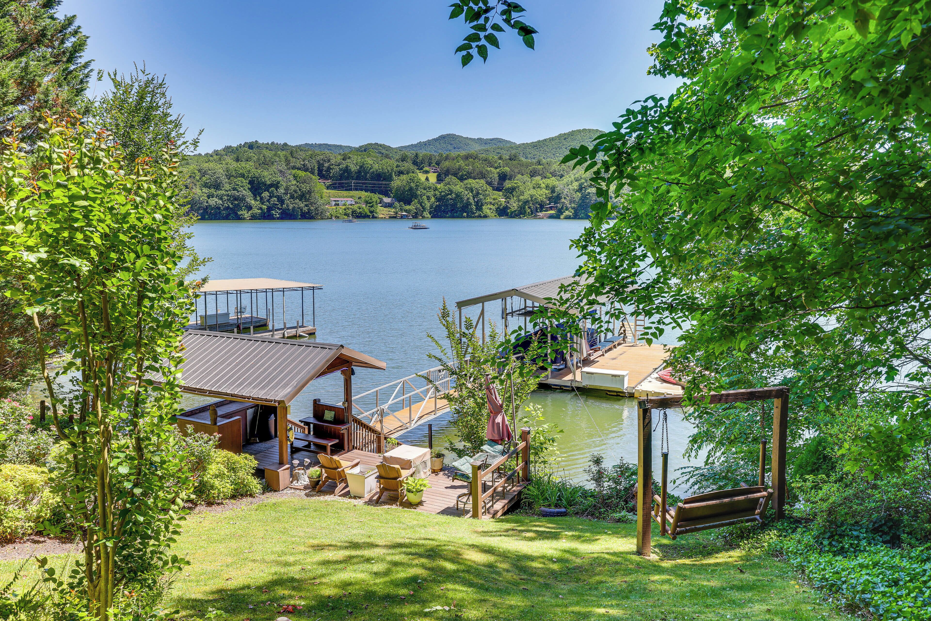 A lakeside property with a wooden deck, outdoor seating, and a swing chair.