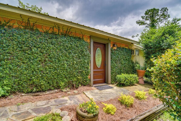A house with a wooden door, a stone pathway, and a well-maintained garden with various plants and a large planter. - 'River's Edge' Alabama Gulf Coast Getaway w/ Deck! (Fairhope)