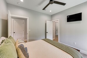 Un dormitorio con cama, almohadas, un ventilador de techo y un televisor instalado en la pared.