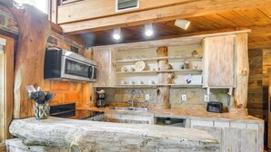 A rustic kitchen with wooden cabinetry, a large log counter, and a microwave. - Riverfront Deck: Outdoor Retreat in Fairhope! (Fairhope)