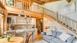 A rustic cabin interior with a dining area, kitchen, and a staircase leading to an upper level. - Riverfront Deck: Outdoor Retreat in Fairhope! (Fairhope)