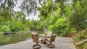 A wooden deck with a table and chairs overlooking a body of water, surrounded by lush greenery. - Riverfront Deck: Outdoor Retreat in Fairhope! (Fairhope)