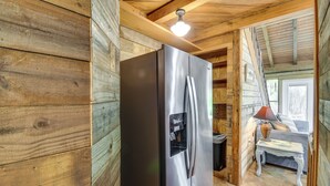 A wooden cabin interior with a stainless steel refrigerator, a wooden ceiling, and a small table with a lamp. - Riverfront Deck: Outdoor Retreat in Fairhope! (Fairhope)