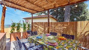 Eine Terrasse im Freien mit einem Esstisch, umgeben von Stühlen und einem Bambuszaun.