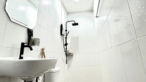 Ett badrum med ett vitt handfat, en spegel, en toalett och en dusch.