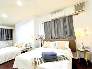 Ein Hotelzimmer mit zwei Betten, einem Nachttisch mit Lampe, einer Wandklimaanlage und einem Fenster mit Vorhängen.