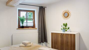 Une chambre à coucher avec un lit, une fenêtre ornée d’une plante, un radiateur, une armoire en bois et un miroir accroché au mur.