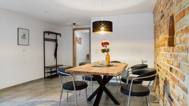 A dining area with a wooden table, black chairs, a hanging light fixture, and a brick wall. - Apartment 'Felicitas' with Wi-Fi (Tann)
