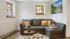 A living room with a sectional sofa, two windows, a painting, and a small table with a candle. - Apartment 'Felicitas' with Wi-Fi (Tann)