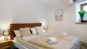A bedroom with a bed, nightstands, a wall-mounted lamp, a framed picture, and a window with a plant. - Apartment 'Felicitas' with Wi-Fi (Tann)
