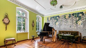Una habitación con un piano de cola, un arpa, un sofá verde y un perro.