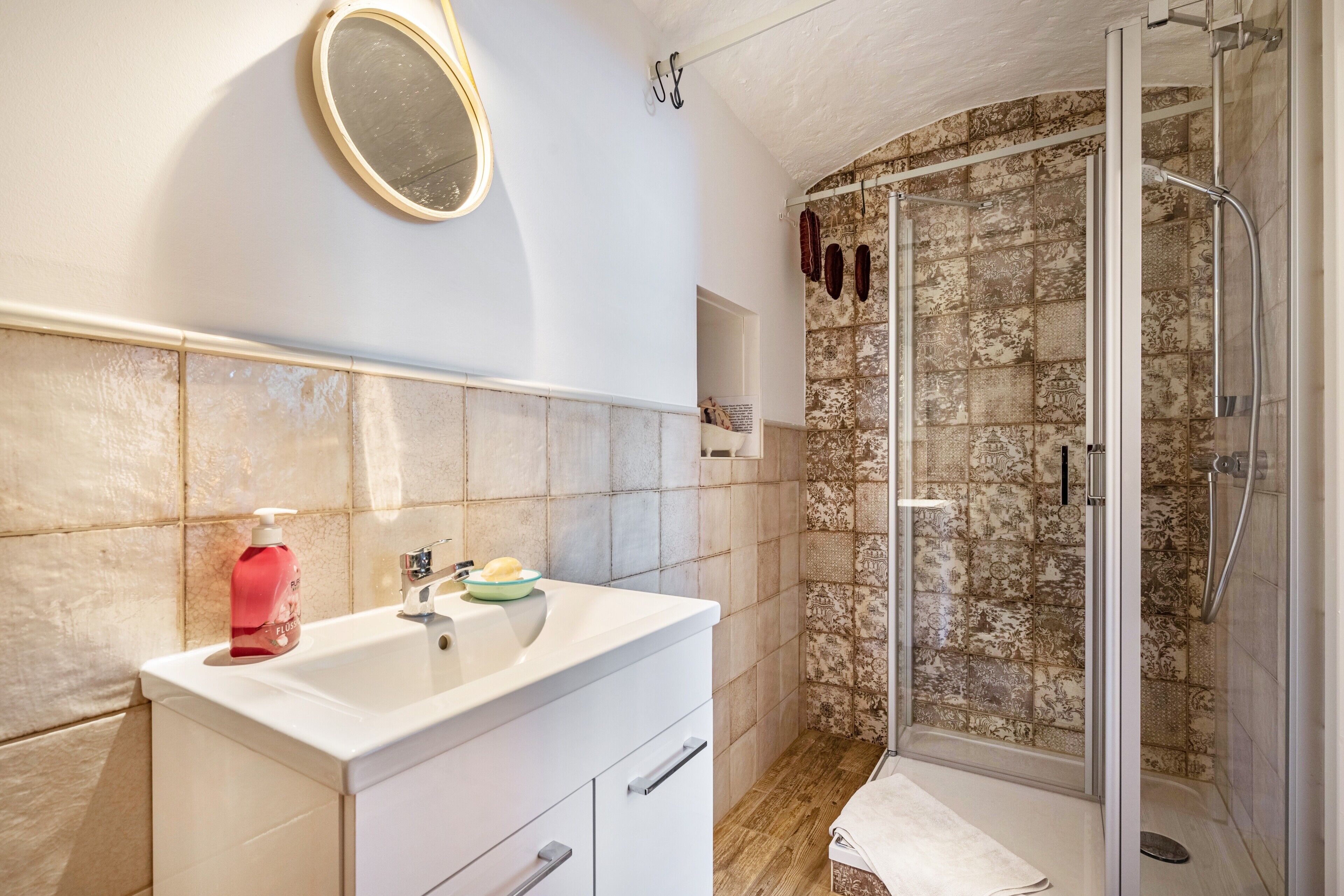Une salle de bain avec un meuble-lavabo blanc, un miroir, une douche avec une porte en verre et des carreaux décorés.