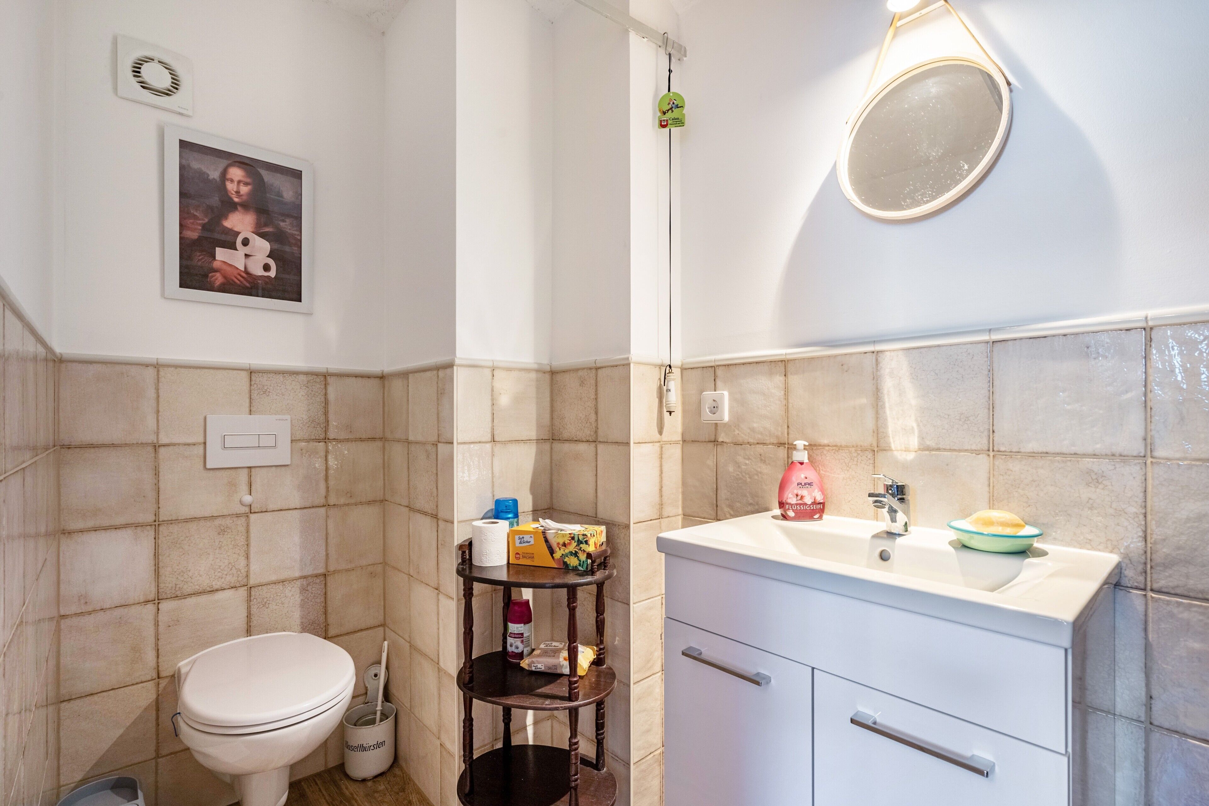 A bathroom with a toilet, sink, mirror, and a shelf with toiletries.