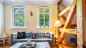 Una habitación acogedora con un sofá, una mesa de madera con velas y dos ventanas con vistas al verdor.