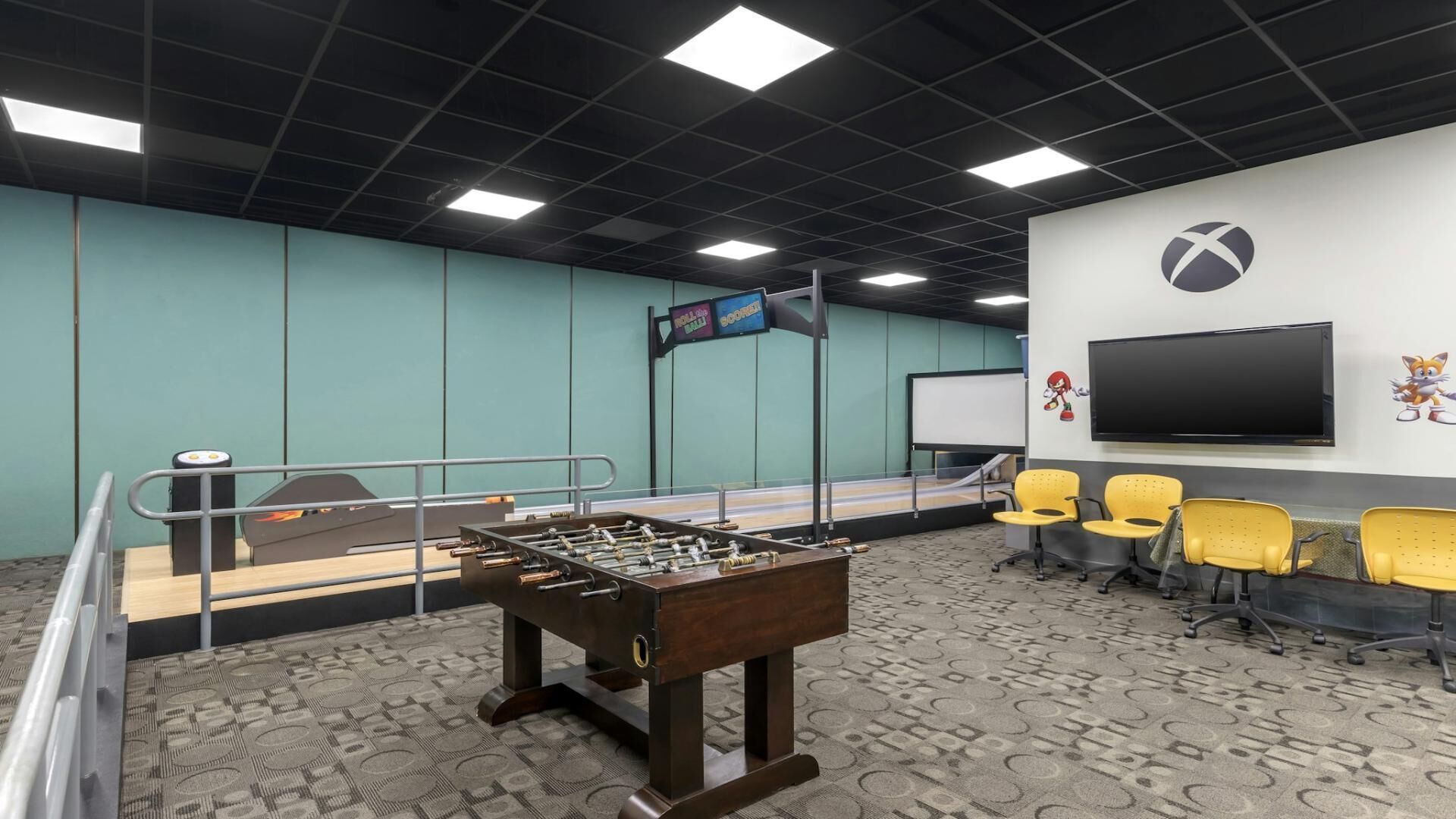 A room with a foosball table, a TV, and yellow chairs.