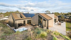 A modern house with a large deck, a hot tub, and a solar panel roof. - 4 bedroom pet friendly home in Blokhus (Blokhus)