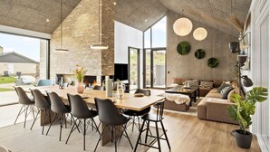 A modern interior with a large dining area, a cozy seating area, and a fireplace. - 4 bedroom pet friendly home in Blokhus (Blokhus)