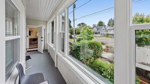 A covered porch with a view of a residential street, a door leading to an interior space, and a chair. - #StayinMyDistrict Historic Heritage Walk to Bay (Coos Bay)
