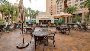 Un espace extérieur aménagé en terrasse, avec plusieurs tables et chaises rondes, entouré de palmiers et agrémenté de parasols.