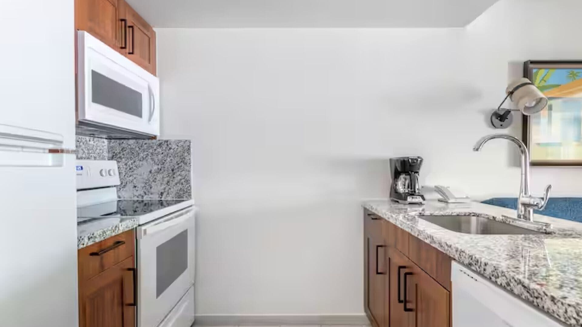A compact kitchen with a microwave, stove, coffee maker, and sink.