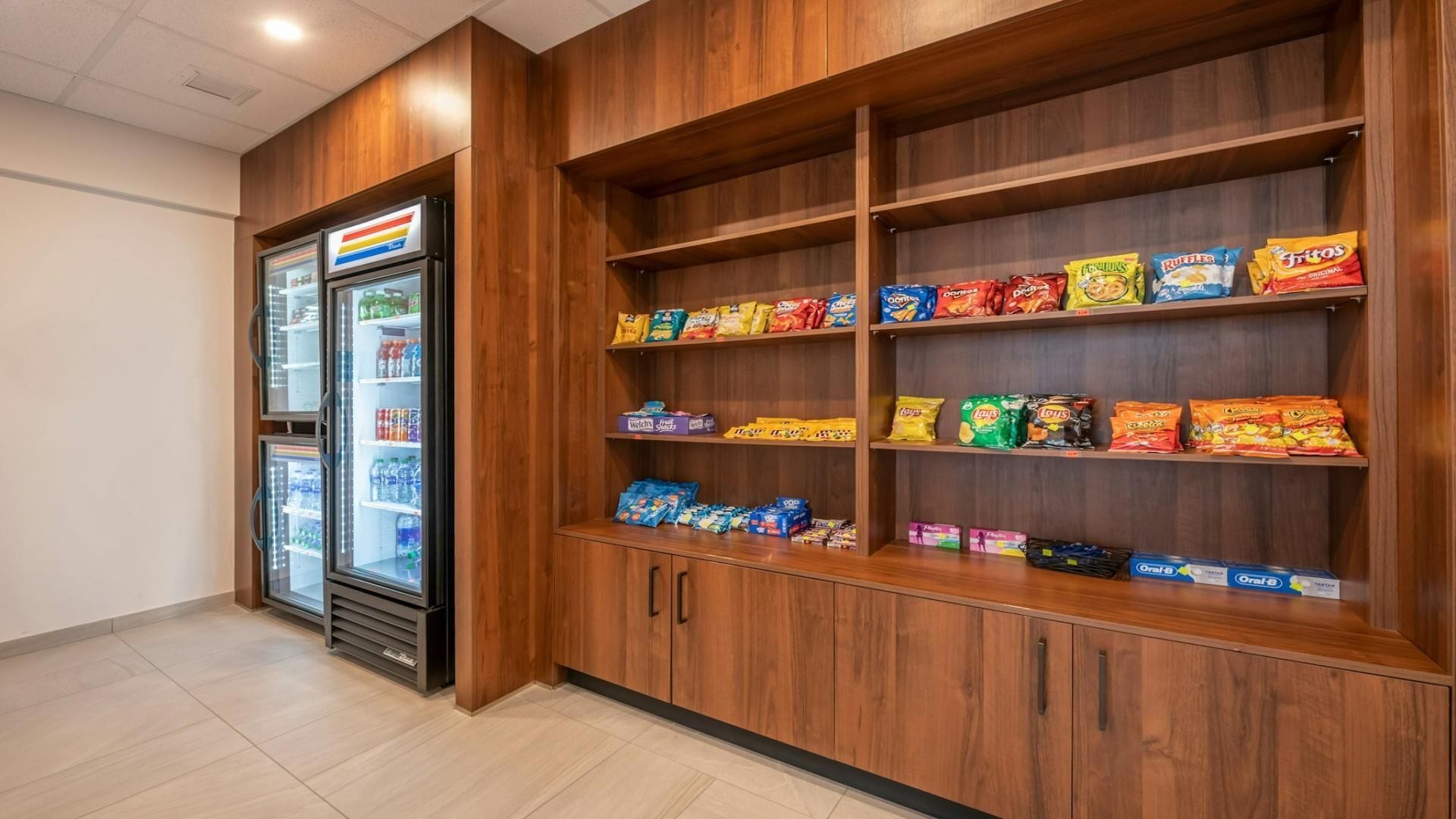 Una presentación de aperitivos con papas fritas y otros bocadillos, un refrigerador con bebidas, y estanterías de madera.