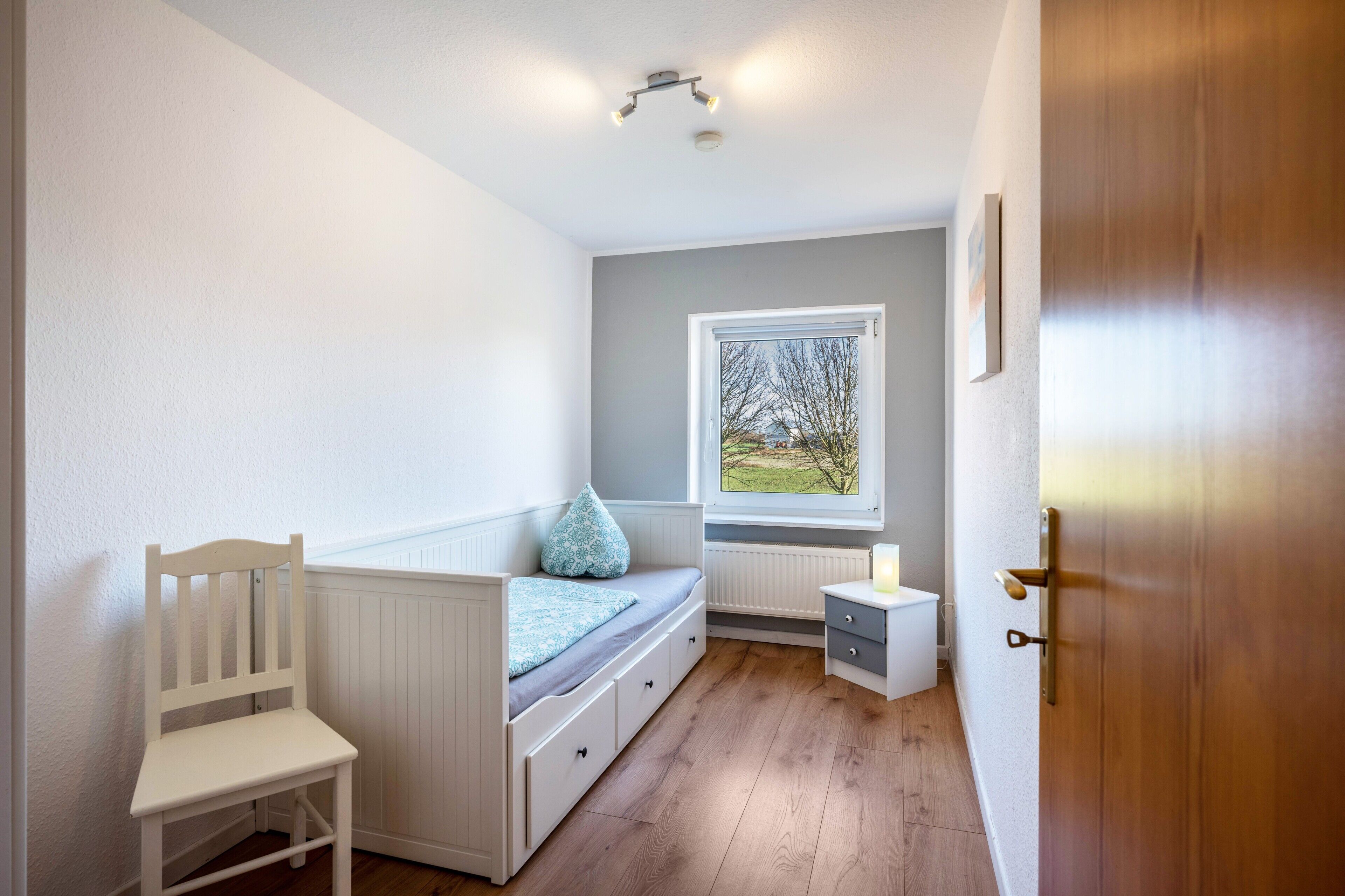 Habitación infantil con literas, una silla pequeña, una mesita de noche, una ventana con vistas y una puerta.