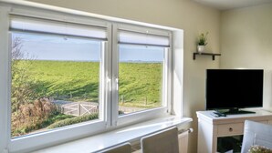 Ein Zimmer mit einem großen Fenster, das Blick auf ein grünes Feld und eine entfernte Landschaft bietet.