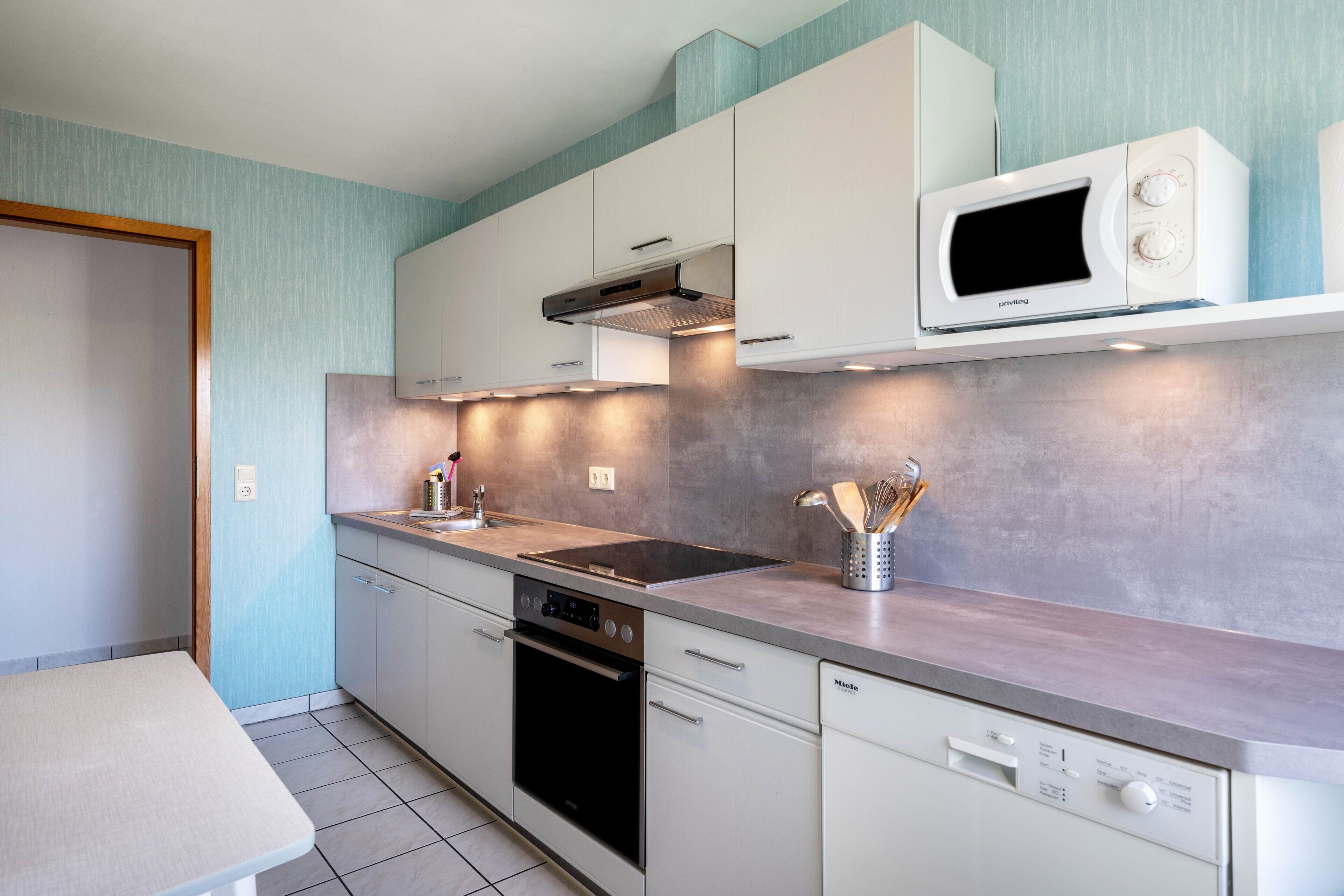 Una cucina moderna con mobili bianchi, forno a microonde integrato, piano cottura e lavastoviglie.