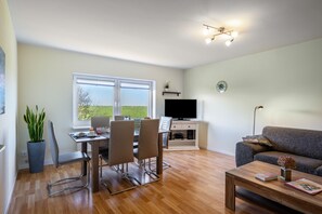 Sala de estar moderna com área de jantar, televisão de tela plana e uma grande janela com vista para o exterior.