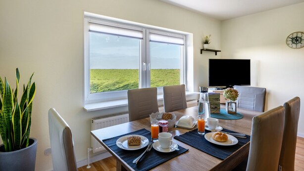 Ein Essbereich mit Tisch, gedeckt für ein Frühstück, einem großen Fenster mit Ausblick, einem Flachbildfernseher und einer Topfpflanze.